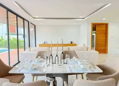 Modern open-plan living room with elegant dining area and pool view, featuring sleek furniture and natural light.