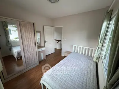 Cozy bedroom with wooden flooring and large window for natural light.