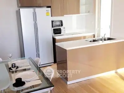 Modern kitchen with sleek cabinetry and dining area, featuring stainless steel appliances and a glass-top table.