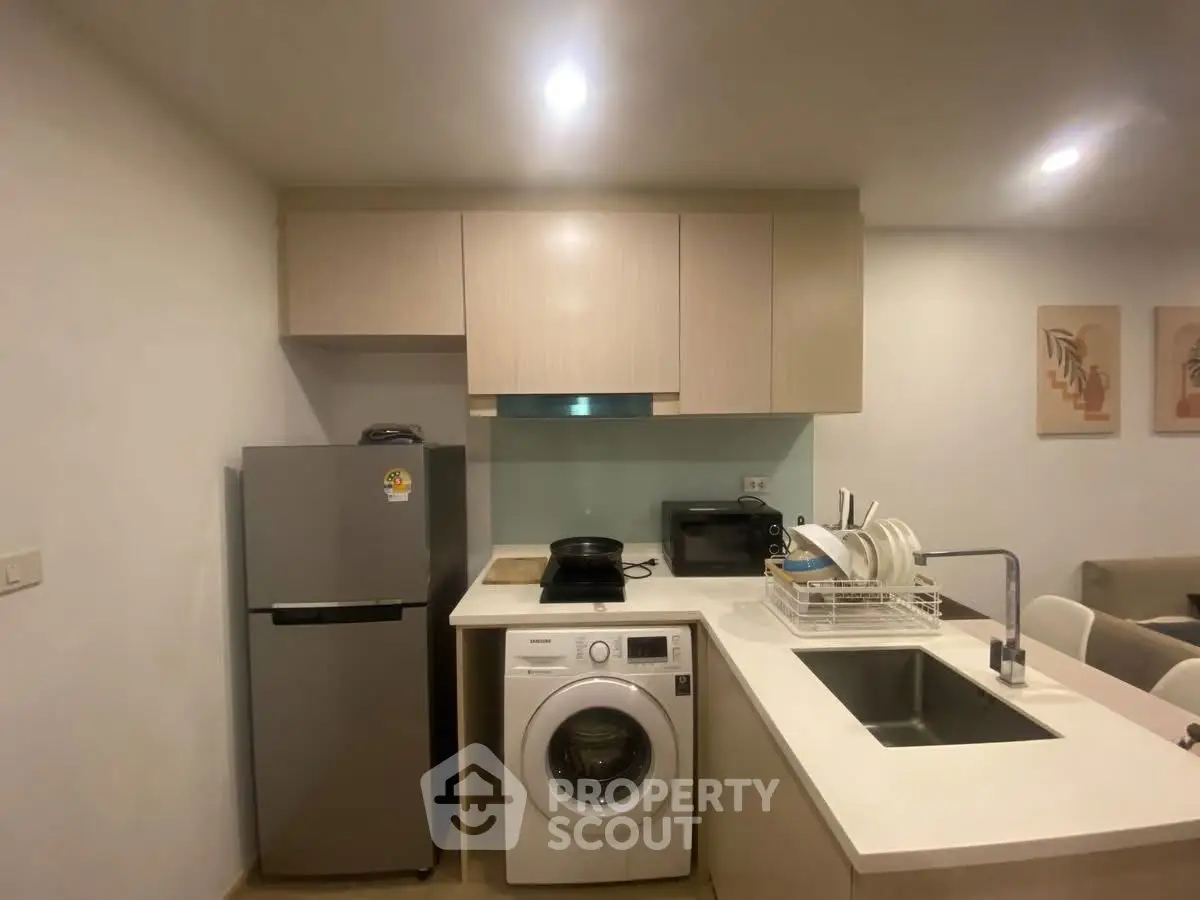 Modern kitchen with washing machine, fridge, and sleek cabinetry in a cozy apartment setting.