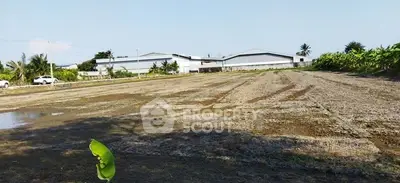 Expansive land plot with potential for development, surrounded by greenery and nearby structures.