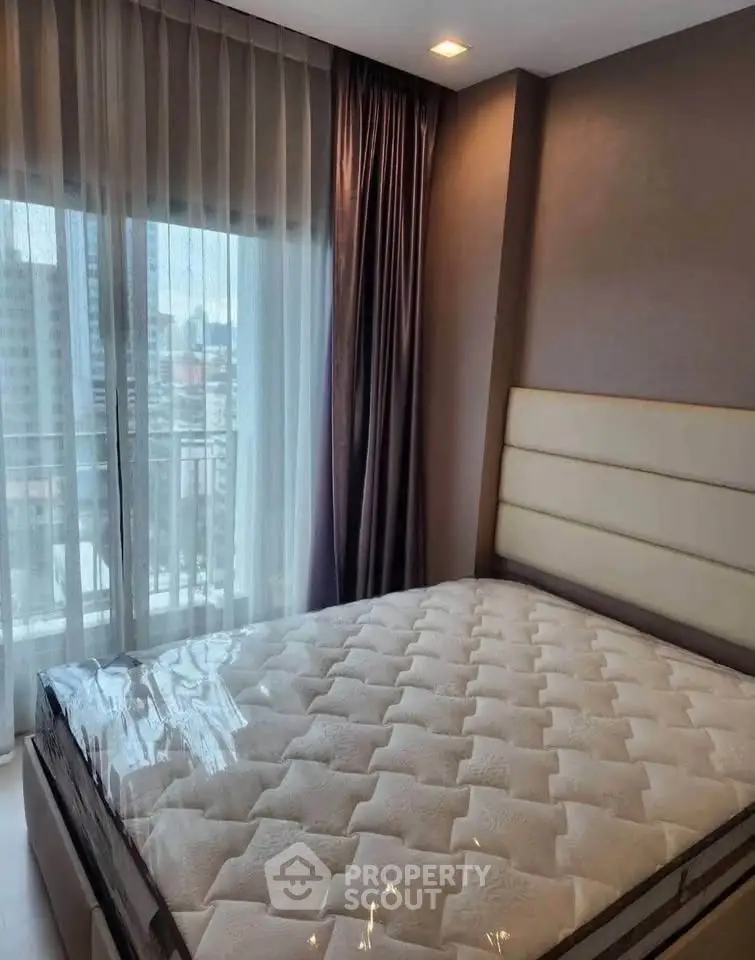 Modern bedroom with large window and city view, featuring a comfortable bed and elegant curtains.