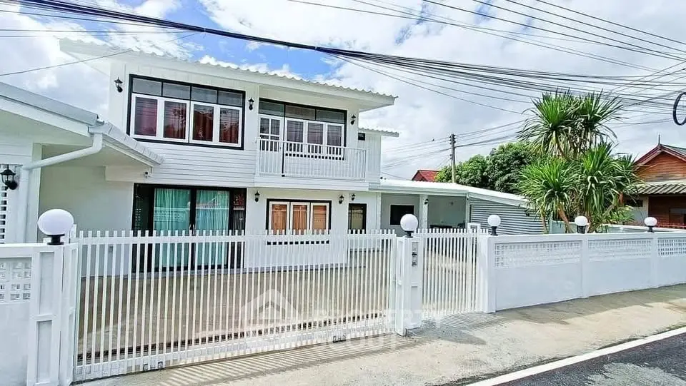 Charming two-story white house with gated driveway and lush greenery.