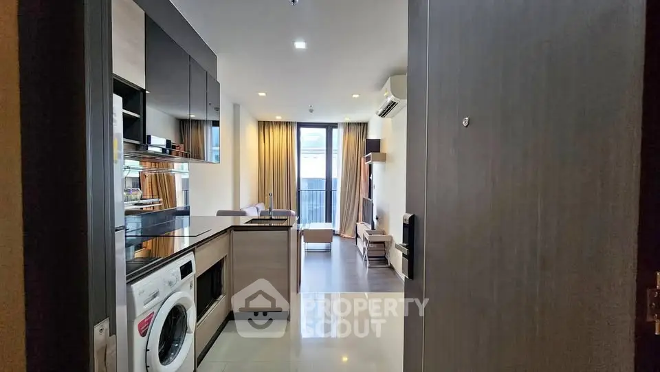 Modern open-layout apartment with sleek kitchen and cozy living area, featuring a washing machine and stylish decor.