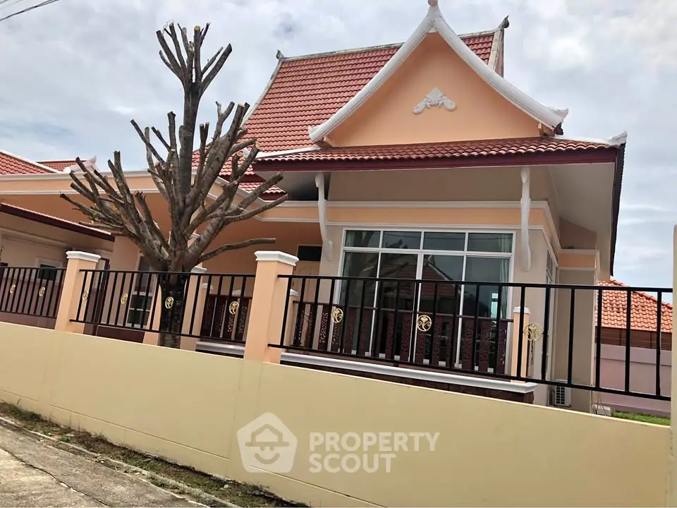 Charming Thai-style house with red-tiled roof and manicured garden, perfect for serene living.