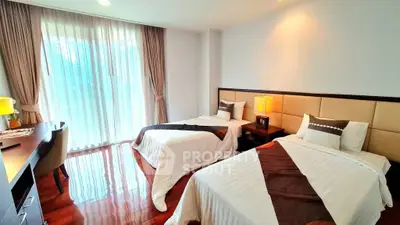 Spacious bedroom with twin beds and elegant decor, featuring floor-to-ceiling windows and polished wooden floors.