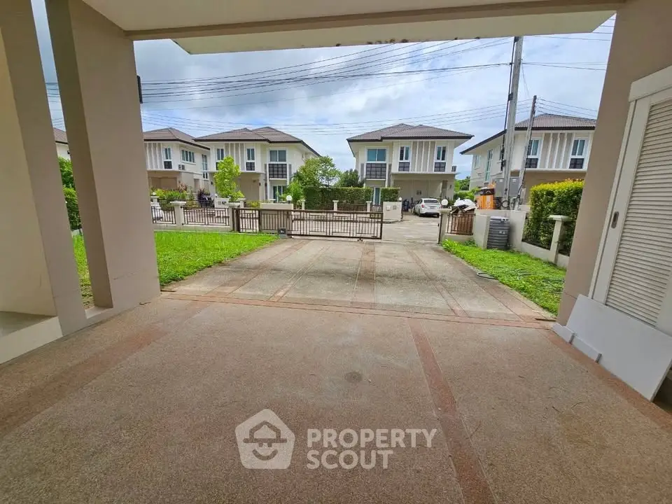 Spacious driveway leading to modern suburban homes with lush greenery and clear skies.