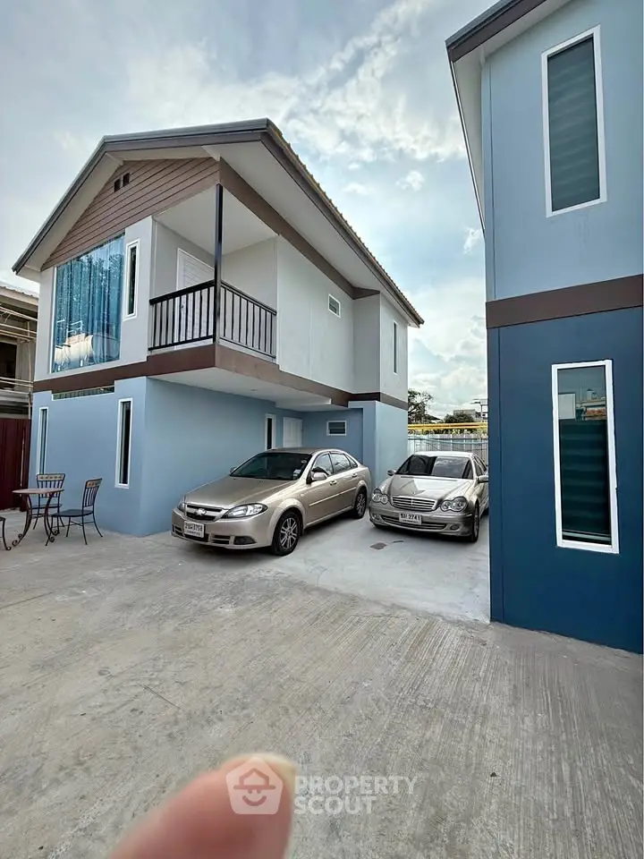 Modern two-story house with driveway and parked cars in a suburban setting.