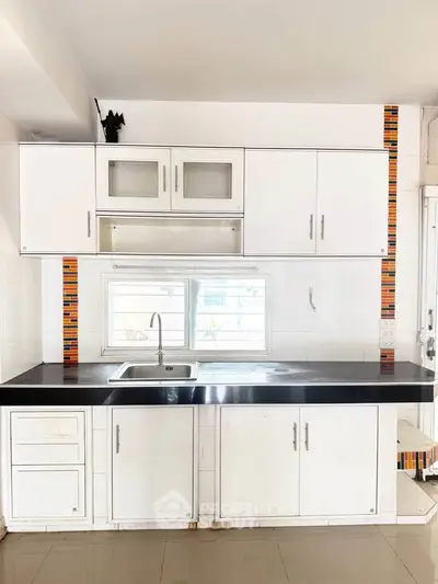 Modern kitchen with sleek white cabinets and black countertop, featuring a stylish backsplash.