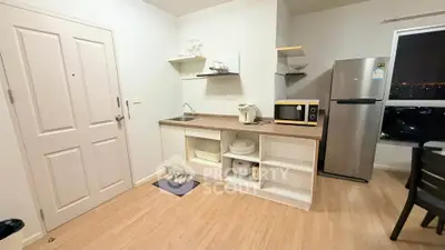 Modern compact kitchen with wooden flooring and sleek appliances in cozy apartment.