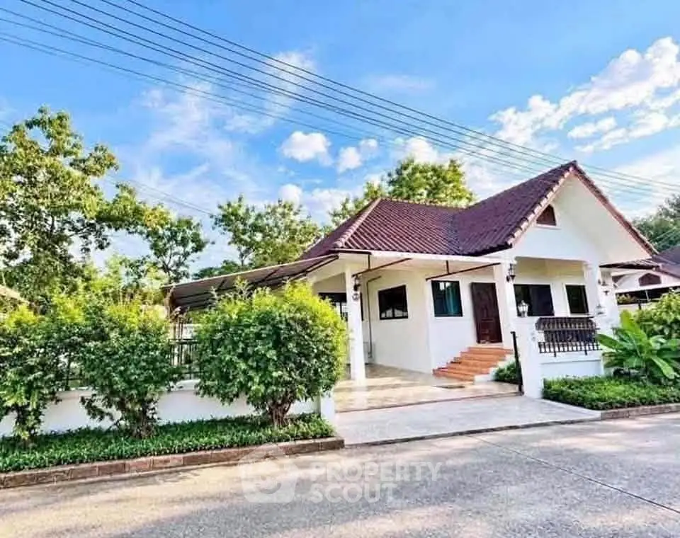 Charming single-story house with lush greenery and spacious driveway under a clear blue sky.