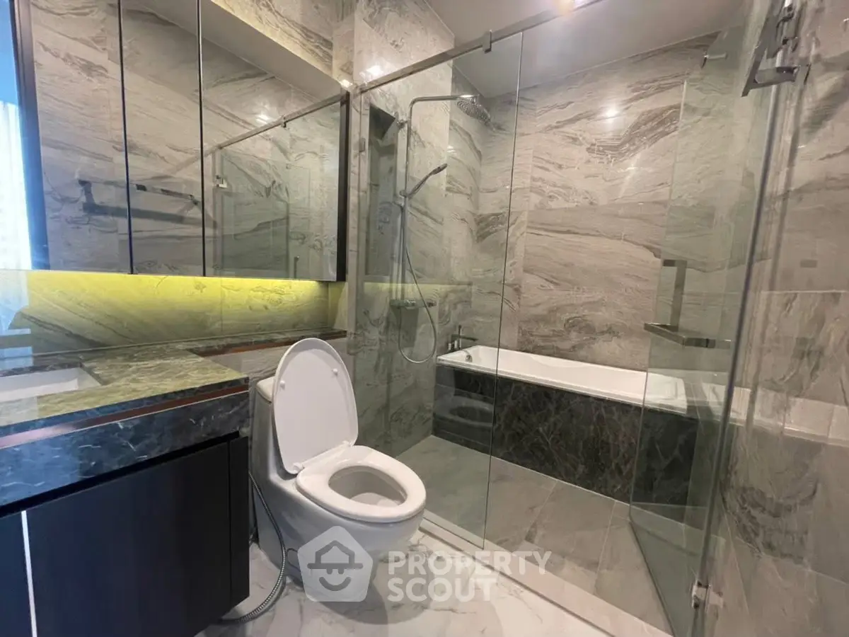 Luxurious modern bathroom with marble finishes and glass shower enclosure.