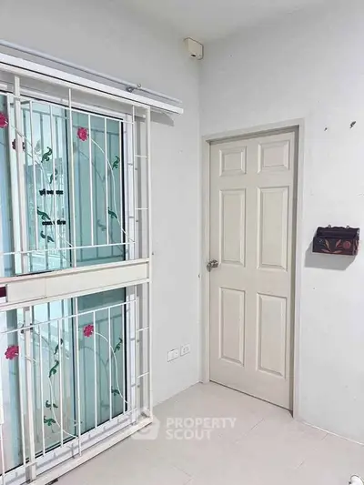 Bright interior corner with window and door, featuring floral window grills.