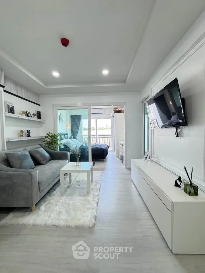 Modern living room with sleek design, cozy gray sofa, and wall-mounted TV, leading to a stylish bedroom.