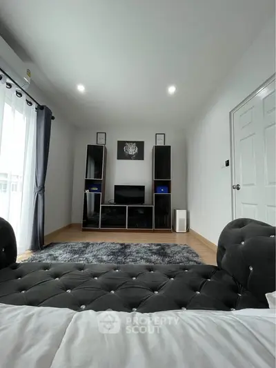 Modern living room with plush black sofa, stylish entertainment center, and natural light from large windows.