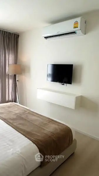 Modern bedroom with air conditioning and wall-mounted TV, featuring cozy bedding and natural light.