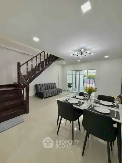 Modern dining area with elegant staircase and cozy seating in a stylish home.