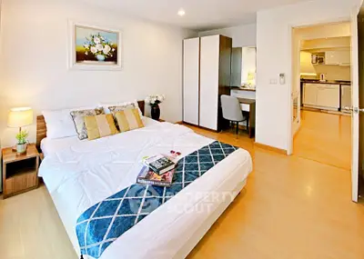 Spacious bedroom with modern decor and cozy ambiance, featuring a study nook and open access to the kitchen.