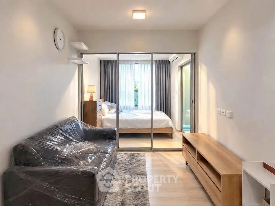 Modern apartment interior with cozy living room and bedroom separated by glass doors.