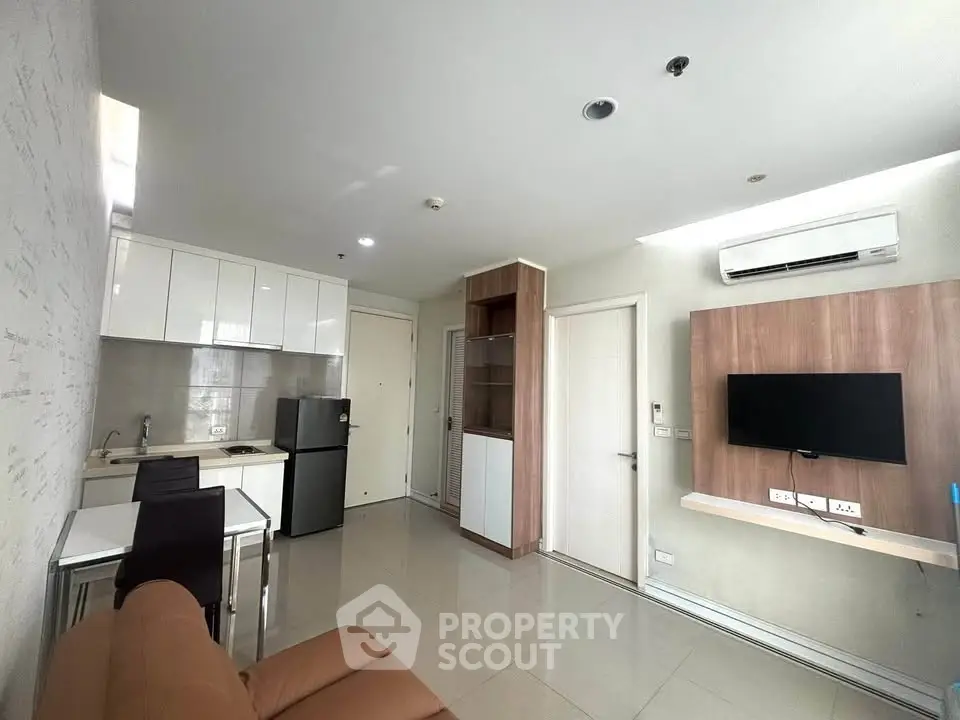 Modern living room with open kitchen, sleek furniture, and wall-mounted TV in a cozy apartment.