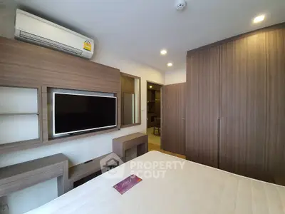 Modern bedroom with built-in wardrobe and wall-mounted TV in stylish apartment.