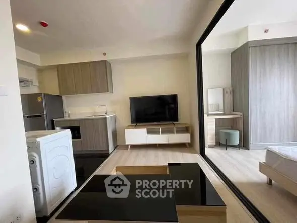 Modern studio apartment with sleek kitchen and cozy living area, featuring a washing machine and flat-screen TV.