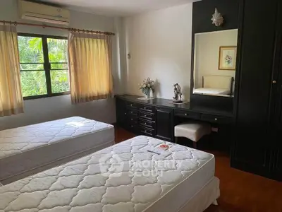 Spacious bedroom with twin beds and elegant black furniture, offering a serene garden view.