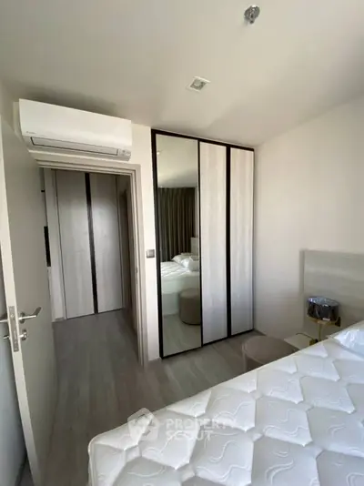 Modern bedroom with mirrored wardrobe and air conditioning unit, featuring minimalist design and neutral tones.
