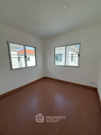 Bright empty room with wooden flooring and two windows offering natural light.