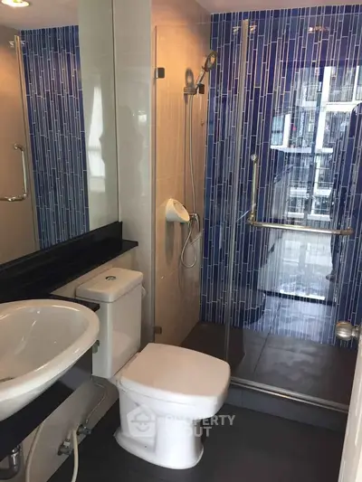 Modern bathroom with glass shower and blue tile accents in a stylish apartment.