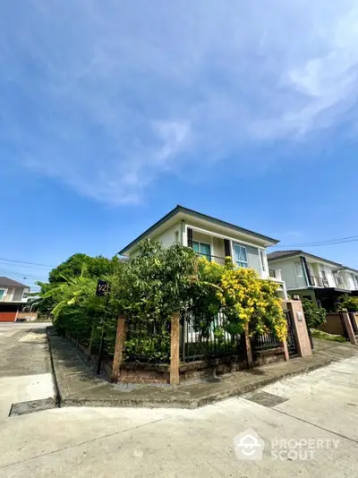 Charming two-story house with lush garden on a sunny day, perfect for family living.