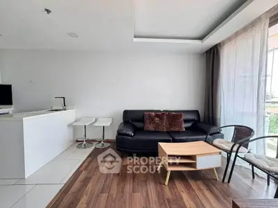Modern living room with sleek black sofa, wooden flooring, and natural light from large windows.
