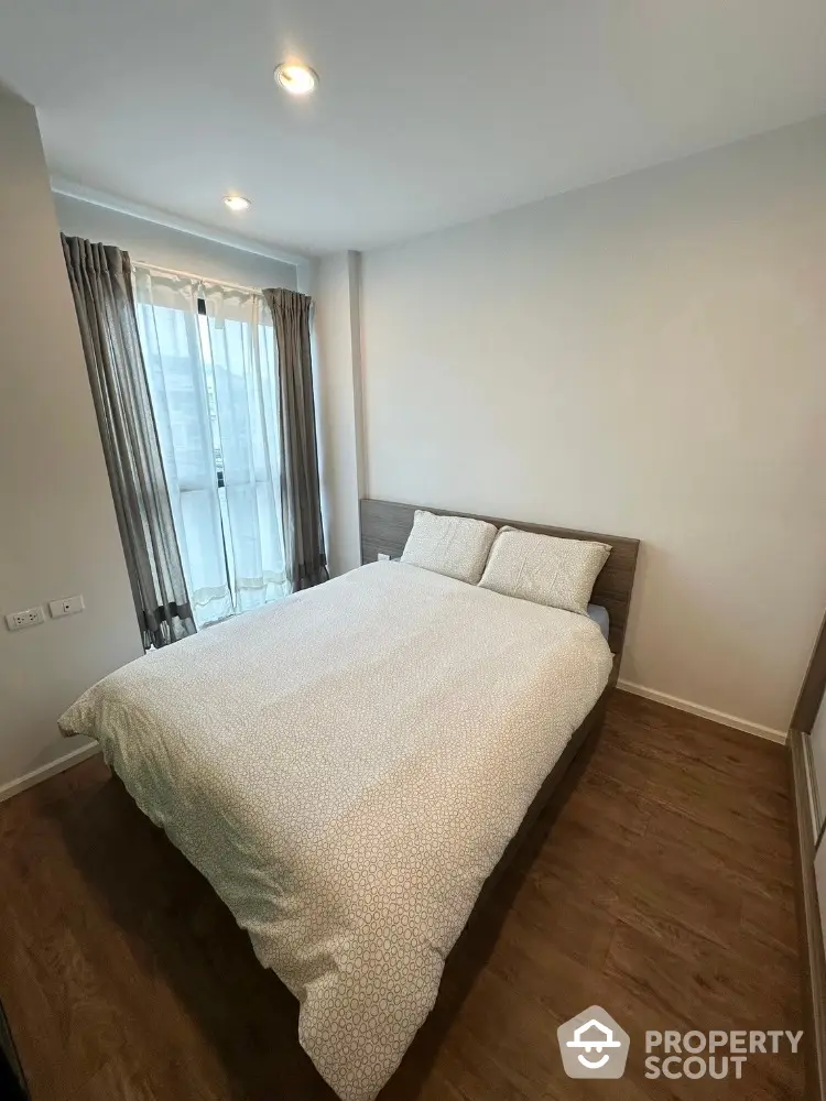 Cozy bedroom with wooden flooring and large window for natural light