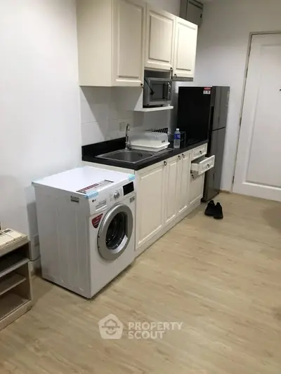Modern kitchen with washing machine, fridge, and sleek cabinetry in compact layout.
