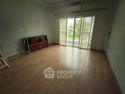 Spacious empty room with wooden flooring and large windows leading to a balcony.