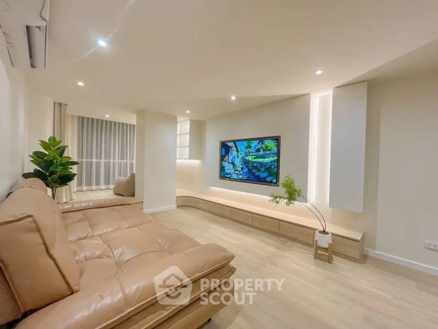 Modern living room with sleek design and large TV, featuring cozy seating and elegant lighting.