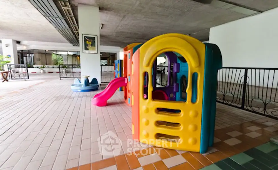Spacious covered play area with colorful children's playground equipment in a modern residential complex.