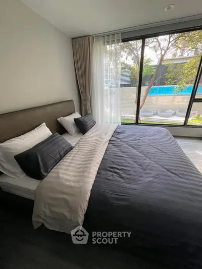 Luxurious bedroom with pool view through large windows, modern decor and cozy bedding.