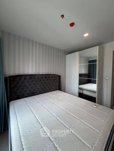 Modern bedroom with stylish headboard and mirrored wardrobe in a cozy apartment.