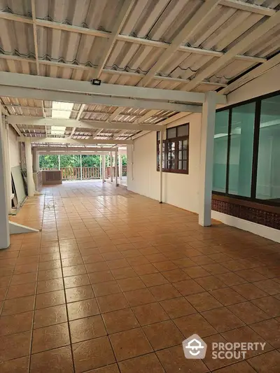 Spacious covered terrace with tiled flooring and large windows, ideal for outdoor gatherings.