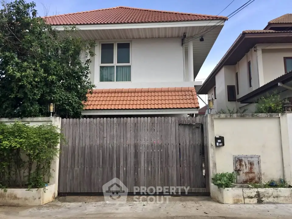 Charming two-story house with red-tiled roof and wooden gate in a serene neighborhood.