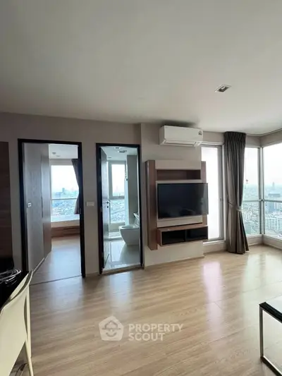 Modern apartment with open living space and city view, featuring sleek wooden flooring and large windows.