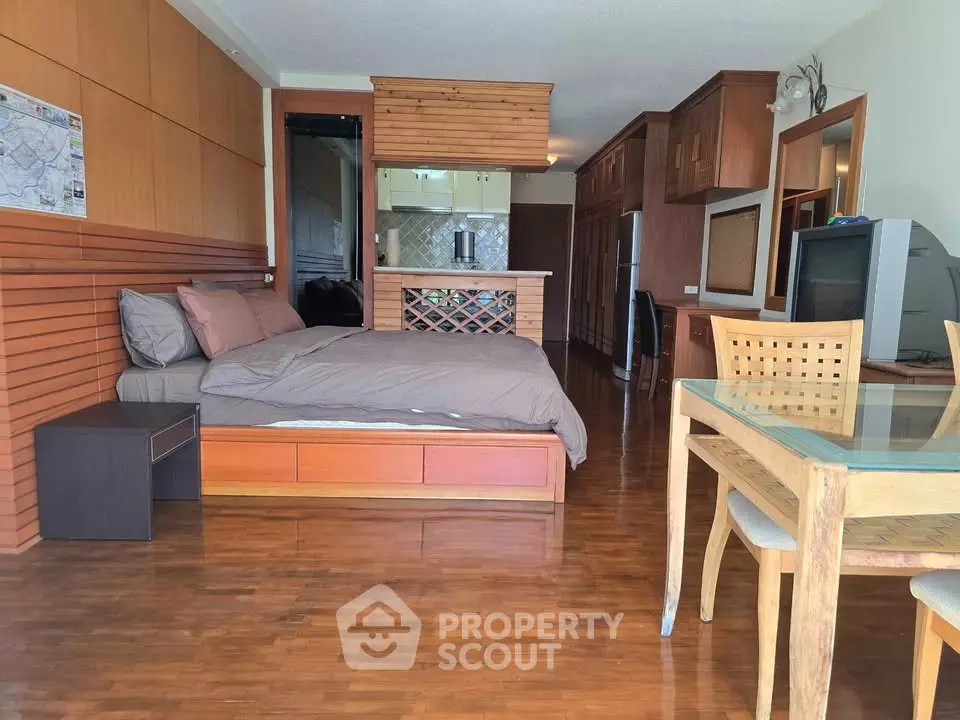Spacious studio apartment with wooden flooring and modern furnishings, featuring a cozy bed and dining area.
