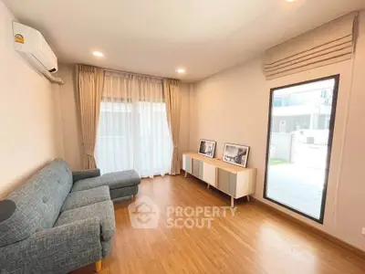 Modern living room with wooden flooring, large window, and stylish furniture in a bright, airy space.
