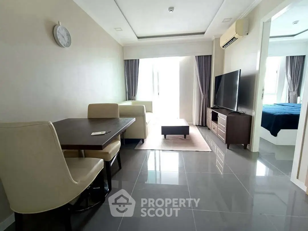 Modern living room with sleek furniture and large TV, adjacent to a cozy bedroom.