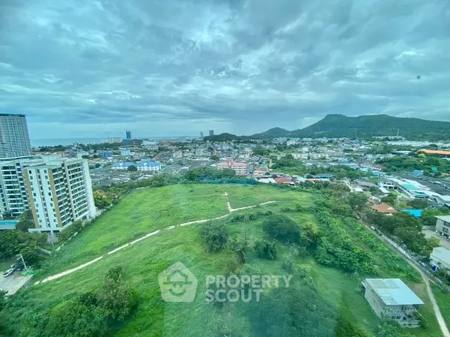 Stunning cityscape view from high-rise building with lush greenery and distant mountains.