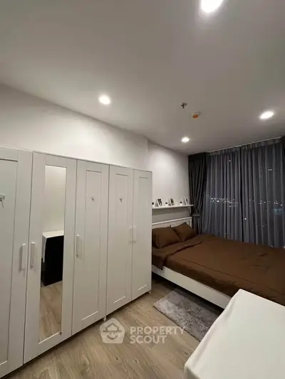 Modern bedroom with sleek white wardrobe and cozy brown bedding, featuring elegant floor-to-ceiling curtains.