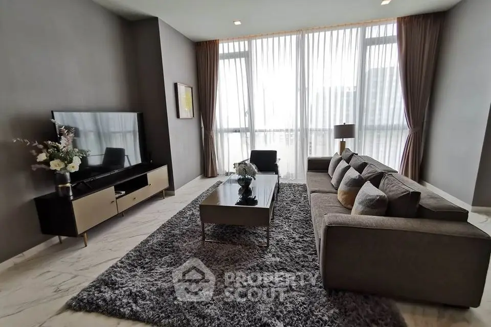 Luxurious modern living room with plush sofa, large TV, and floor-to-ceiling windows.