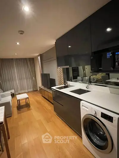 Modern living room with sleek kitchen and built-in washing machine, featuring elegant wood flooring.