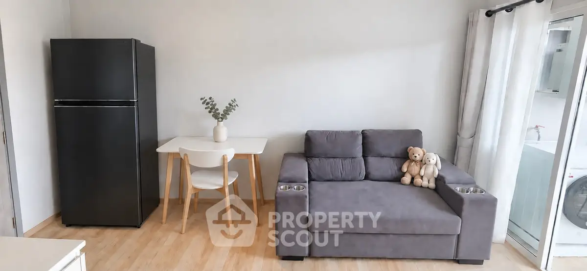 Modern living room with sleek black fridge, cozy gray sofa, and stylish dining area in open layout.